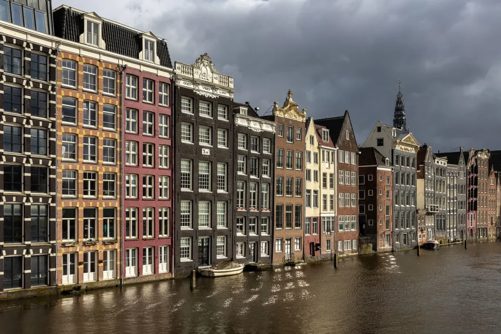 Colourful narrow canal houses along the water at Damrak in Amsterdam