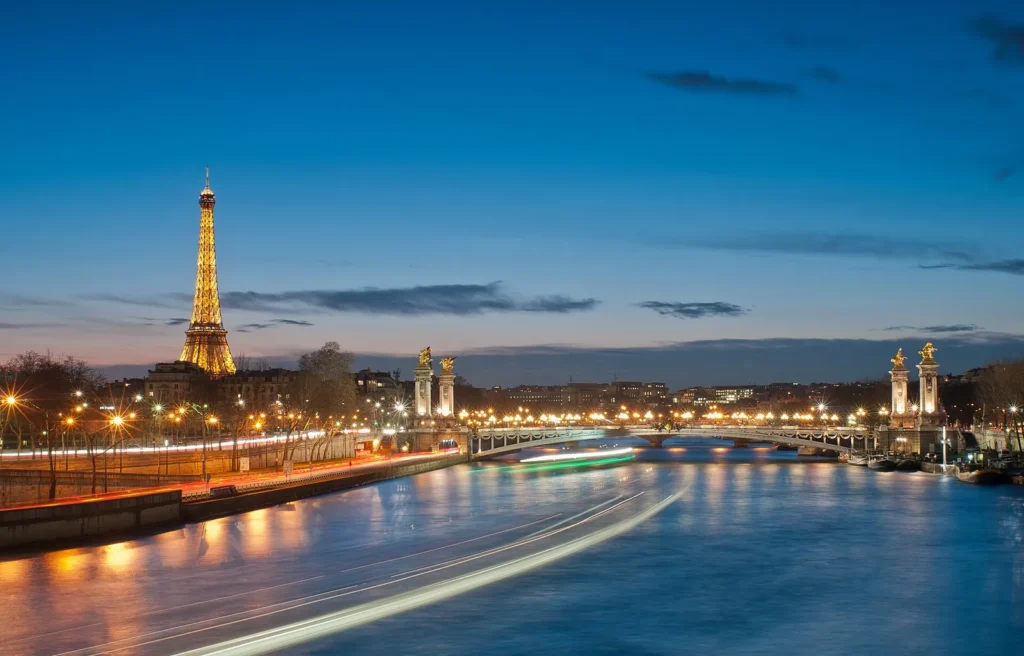 The lit Eiffel Tower beyond the Seine and Pont Alexandre III at dusk