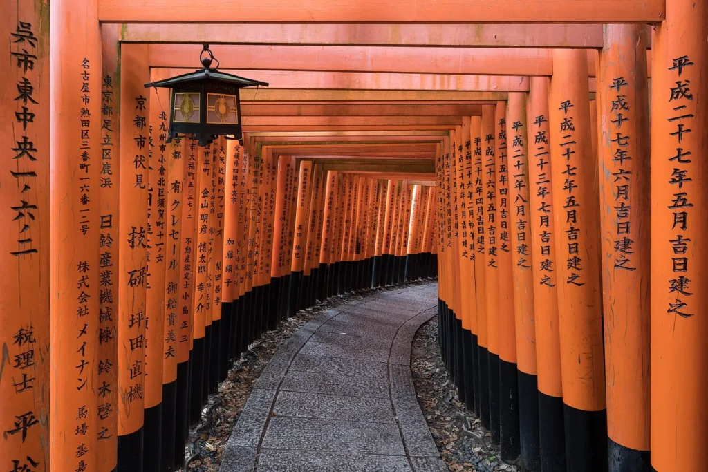 A path lined with orange torii gates and a stone lantern at Fushimi Inari Taisha