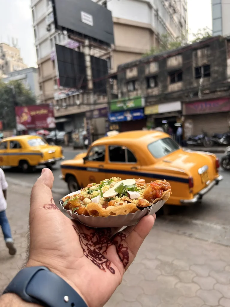Street food stall on a Kolkata pavement with a yellow taxi passing