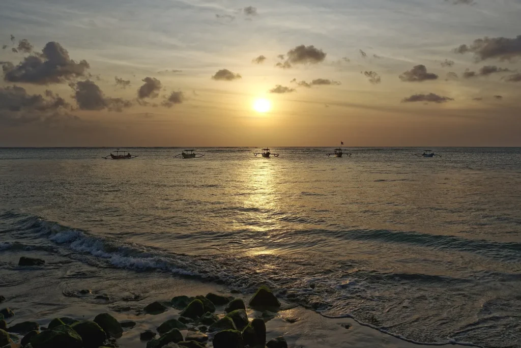 The sun setting over the sea at Kuta beach in Bali with boats on the horizon