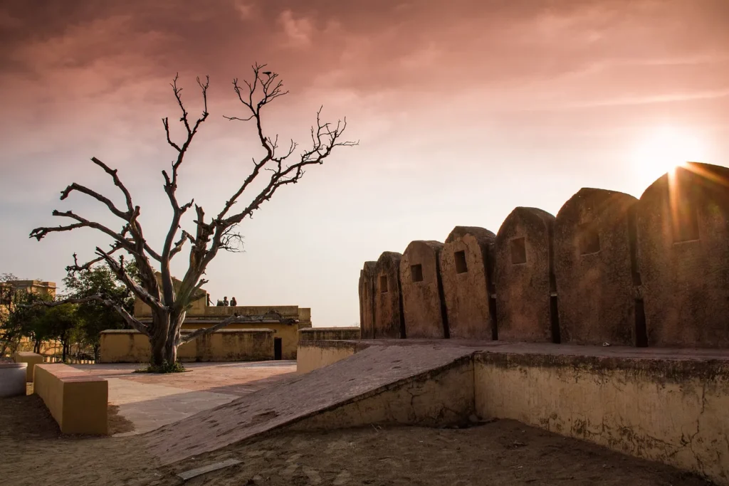 Sun setting behind the crenellated bastion walls of Nahargarh Fort beside a bare tree