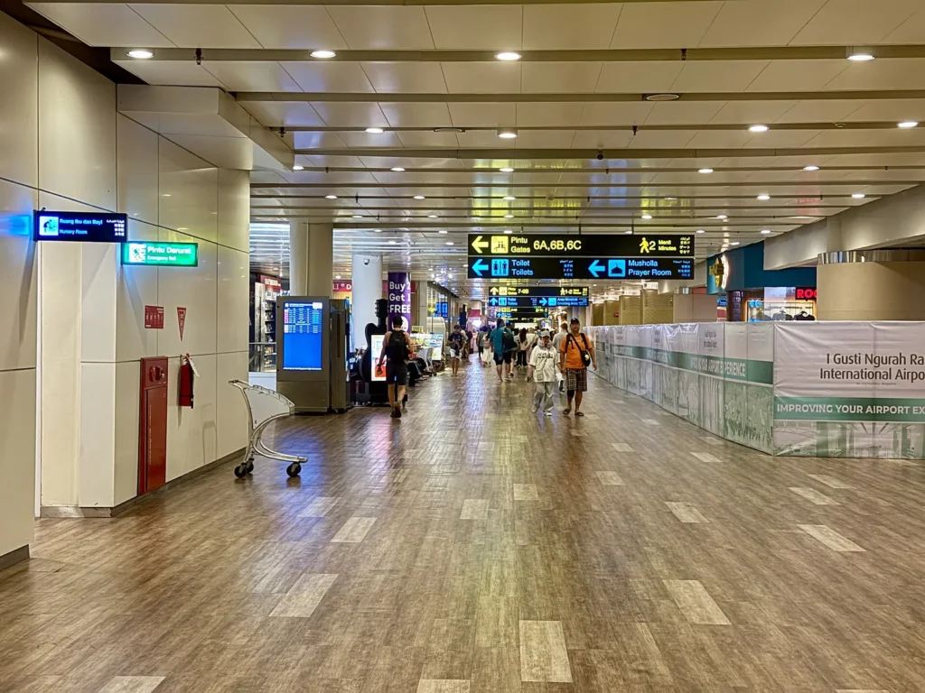Passengers walking along a corridor with overhead direction signs in Ngurah Rai international terminal
