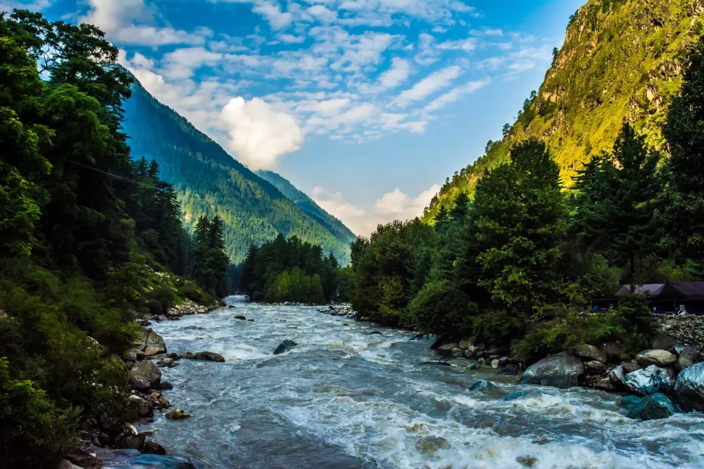 The Parvati river rushing over rocks between forested slopes at Kasol in Himachal Pradesh