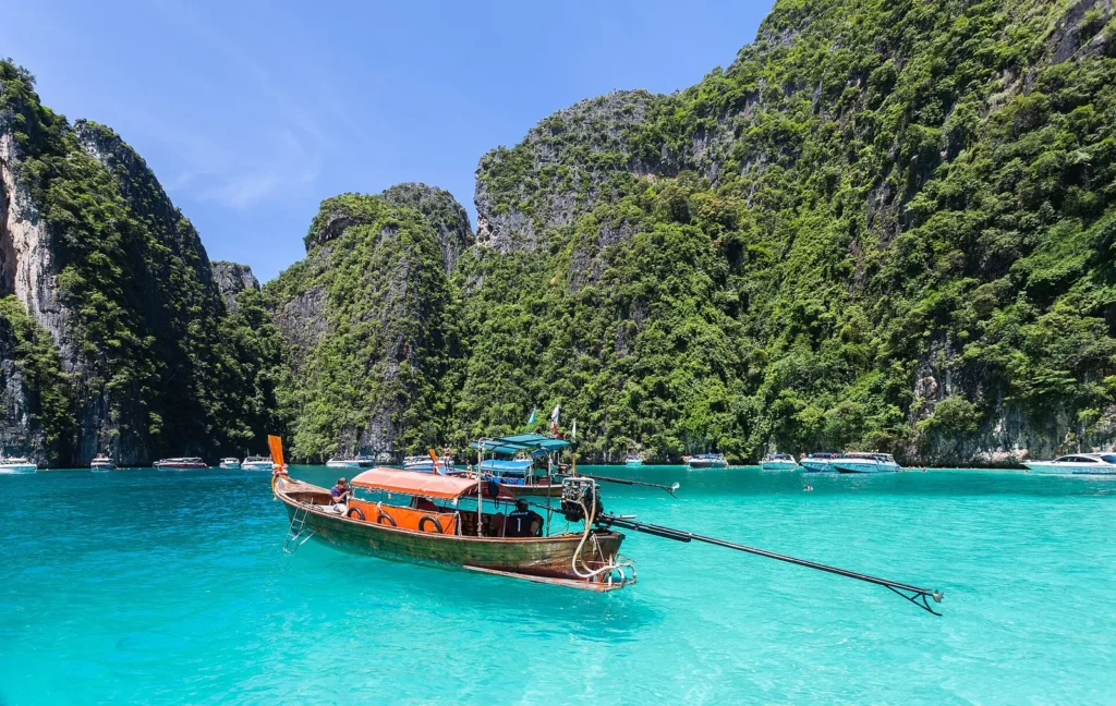 Longtail boats in clear turquoise water below the limestone cliffs of Ko Phi Phi Leh