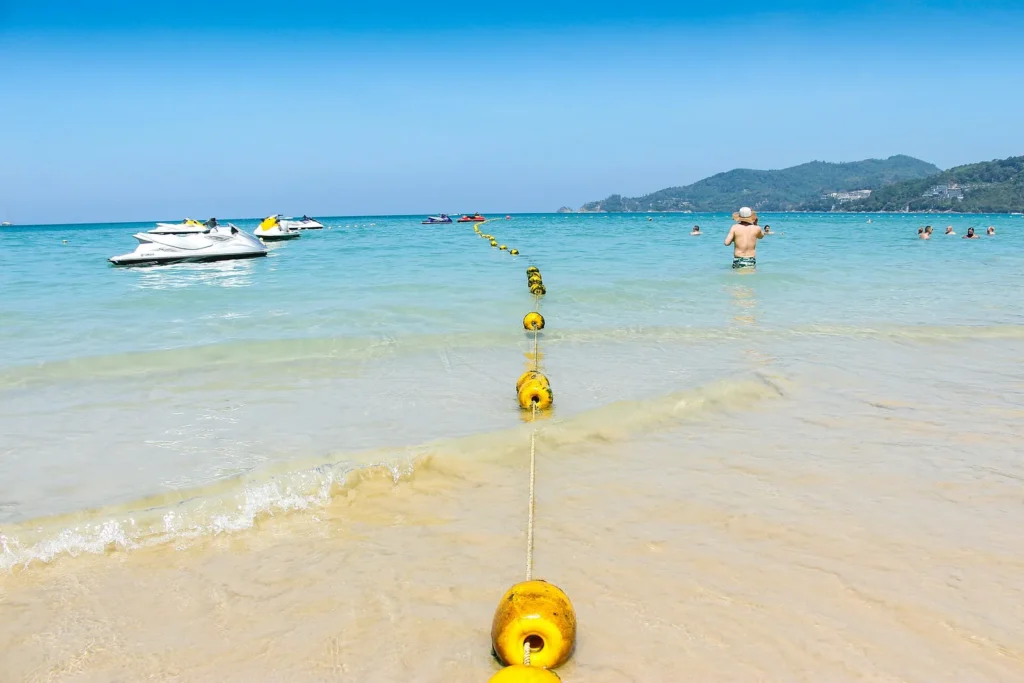 Clear shallow water and a sandy beach in Phuket with boats offshore