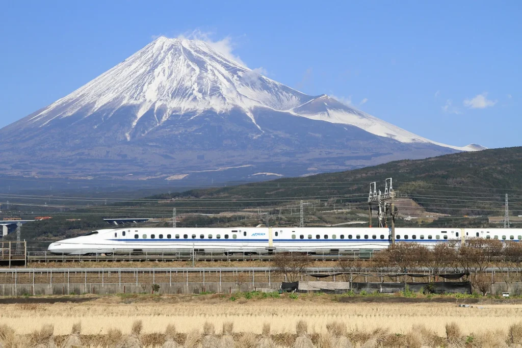 A white N700 series Shinkansen train speeding past with Mount Fuji behind