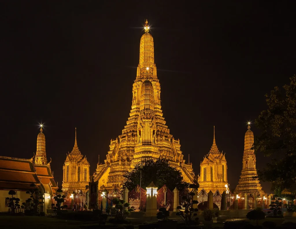 Wat Arun temple in Bangkok lit up in gold at night with its central prang and smaller towers